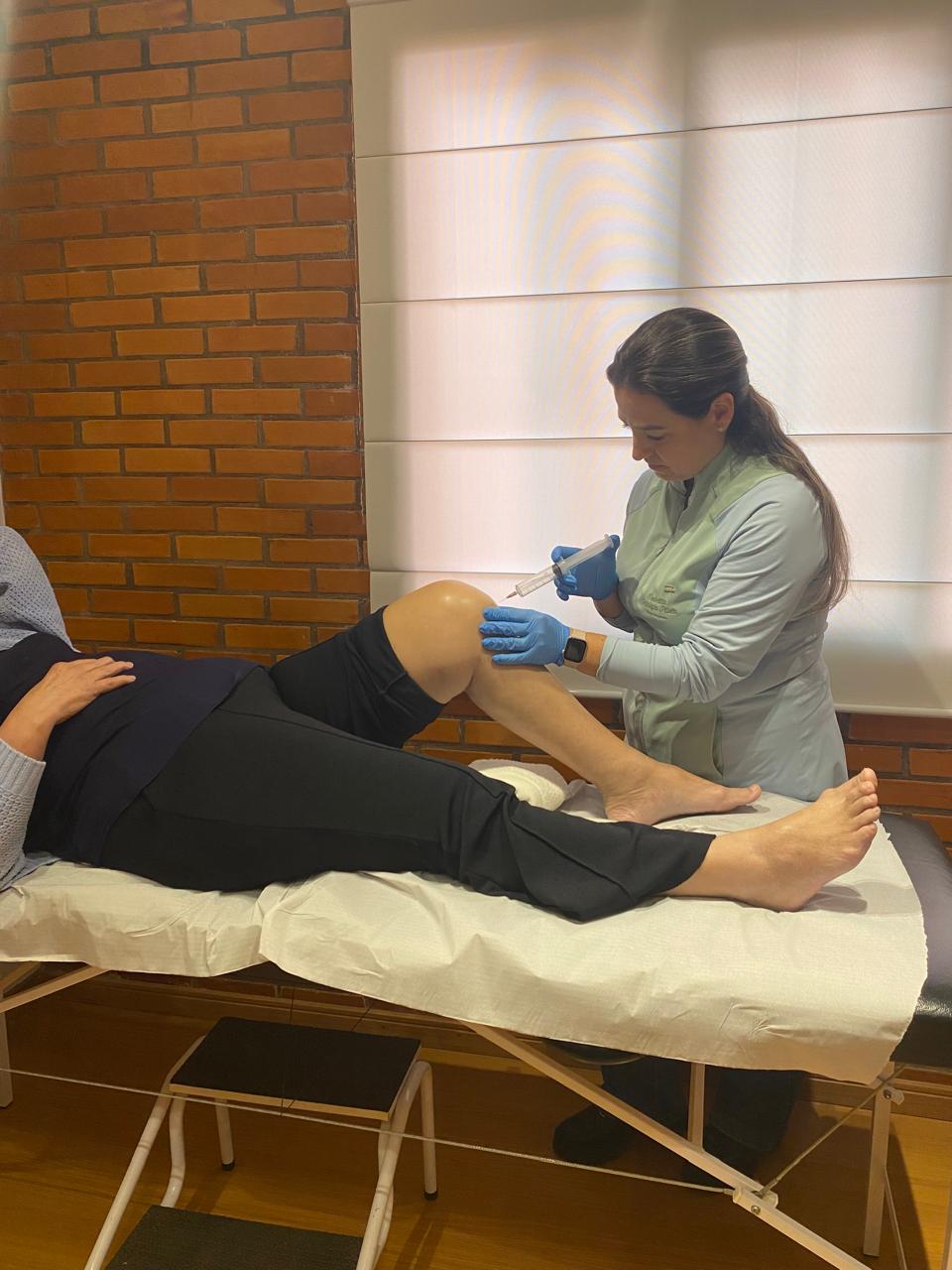 Dra. Isabelita aplicando ozonioterapia no joelho de uma paciente deitada na maca